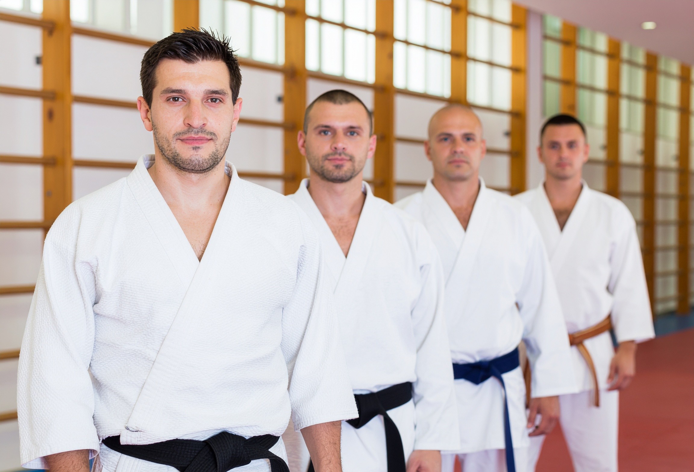 Adult judo students standing in line at Darfight Brooklyn in white gis and black belts, prepared for class